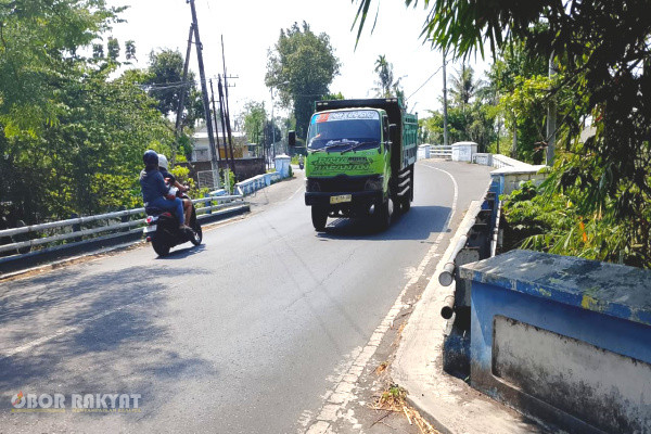 Bondowoso, Obor Rakyat — Imbas domino dari proyek konstruksi Jembatan Sentong di bawah naungan Dinas Pekerjaan Umum (PU) Bina Marga Provinsi Jawa Timur kini memicu persoalan sistemik di Kabupaten Bondowoso. Pengalihan arus lalu lintas (rerouting) ke jalur alternatif lokal tanpa kalkulasi Axle Load (beban muatan sumbu) yang memadai telah mengakibatkan kerusakan masif pada koridor jalan kabupaten hingga memicu kegagalan struktural parsial pada dua jembatan vital.